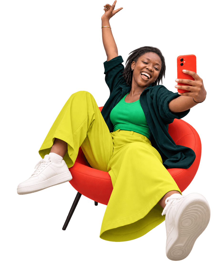 A woman laughing in a red chair, taking a selfie with her phone